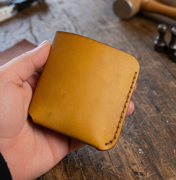 Alt Tag: Compact Bi-Fold Wallet single piece of Maya leather in cognac held in hand, minimalist bi-fold leather wallet with stitched edge