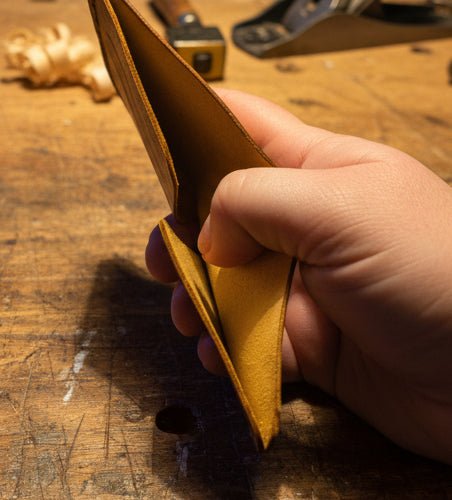 Compact Bi-Fold Wallet single piece of Maya leather in cognac held open by hand, slim profile on workbench